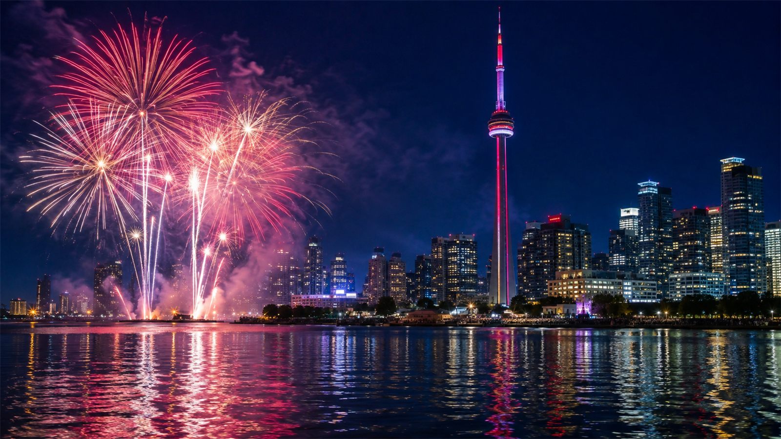 Pink and white fireworks bursting over the Toronto skyline and CN Tower at night, reflected in the lake